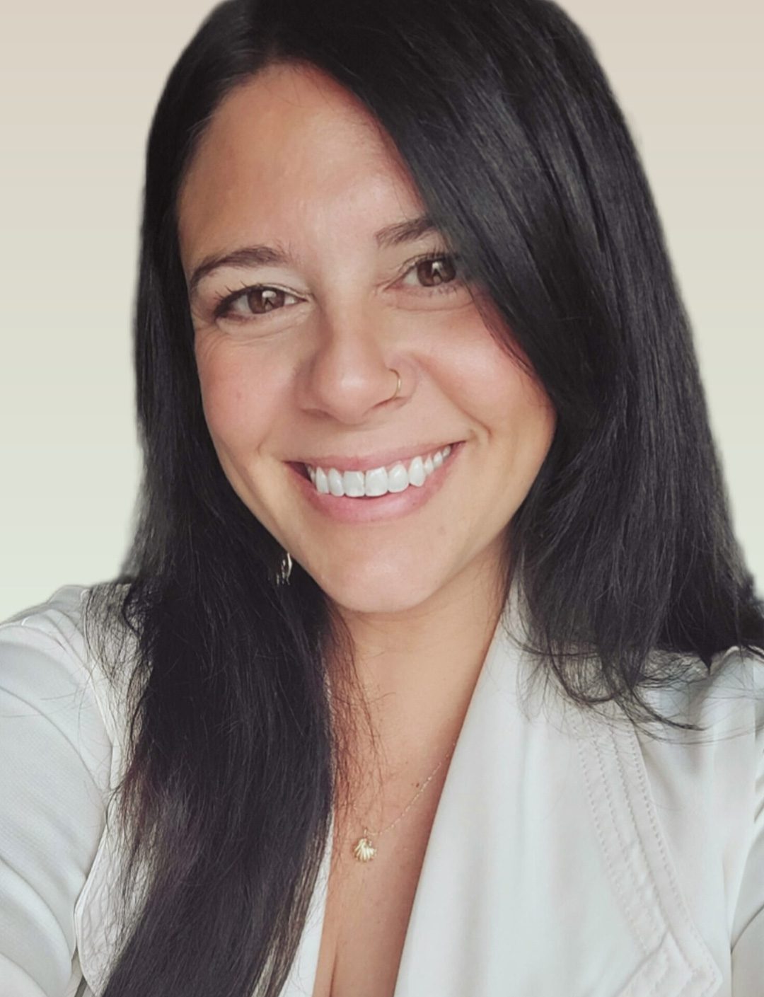 Portrait of a smiling woman with long dark hair wearing a light blouse against a soft gradient background, nose ring visible and a gold necklace.